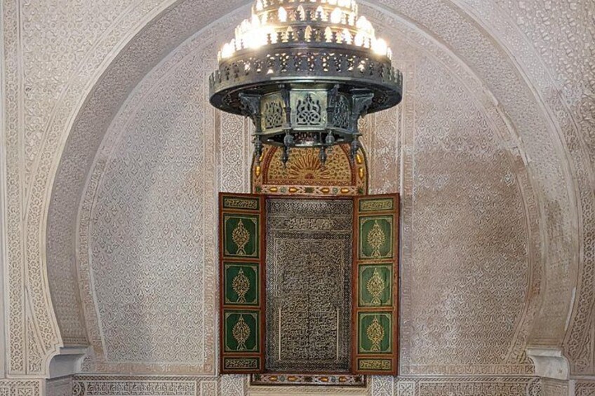An ornate chandelier with intricate designs, a detailed wall panel with calligraphy, and a large arched structure. 5