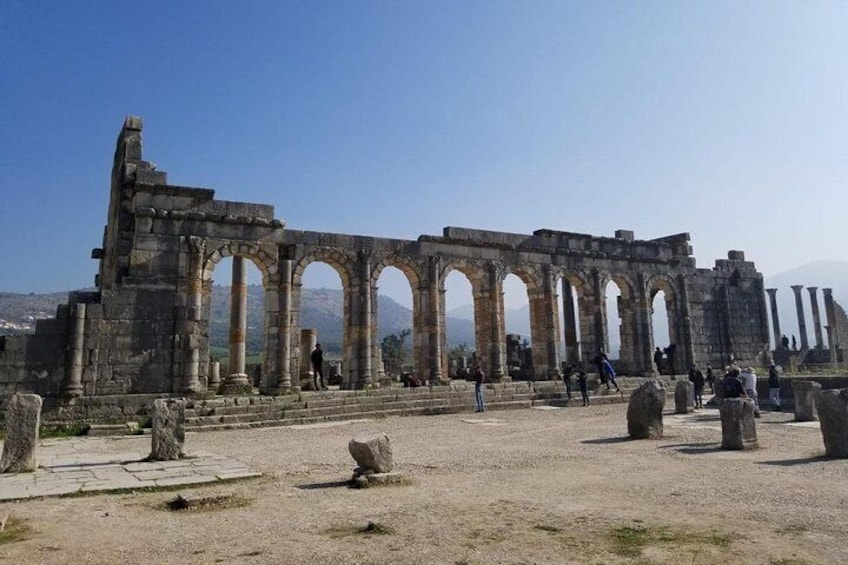 Ancient ruins with arches and columns, a clear sky, and a distant mountain range. 1