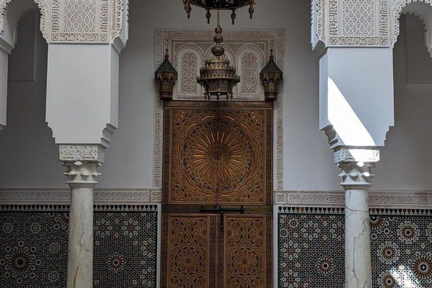 A detailed wooden door with intricate carvings, flanked by white columns with geometric patterns, and a patterned tile wall. 3