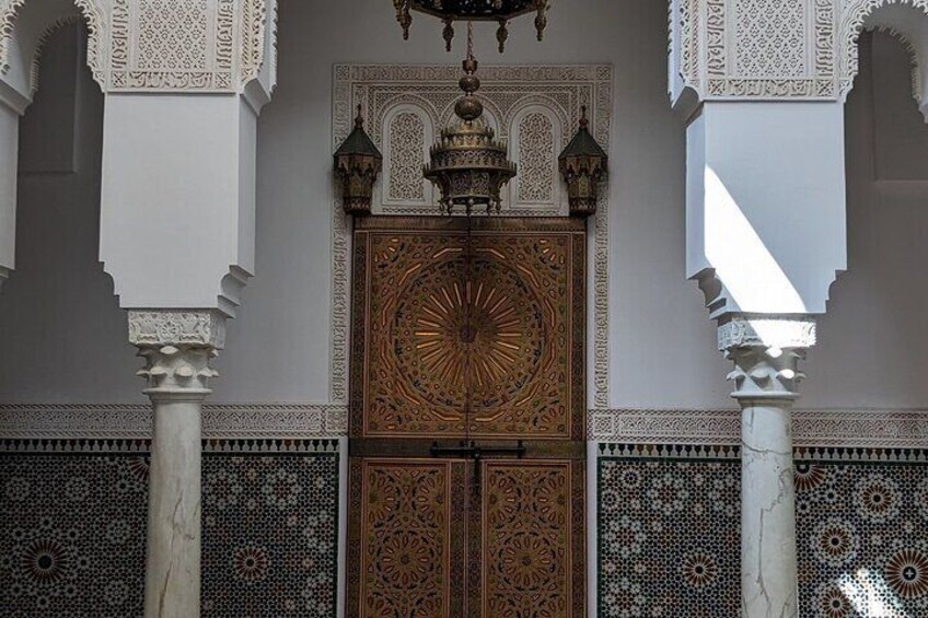 A detailed wooden door with intricate carvings, flanked by white columns and patterned tile walls. 3