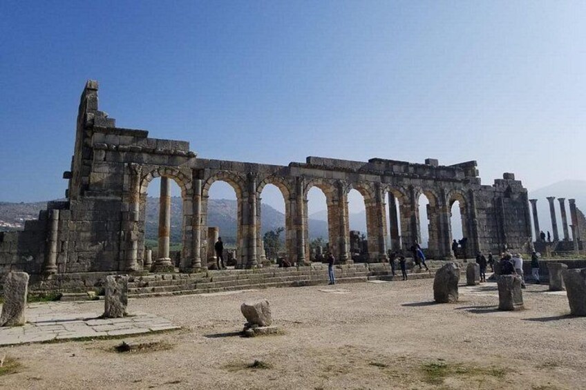Ancient ruins with columns and arches, a clear sky, and a distant mountain range. 1