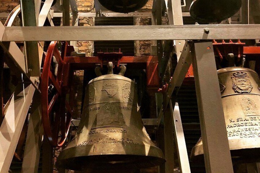 Ein Glockenturm mit einer großen Glocke, Metallstreben und Inschriften. 1