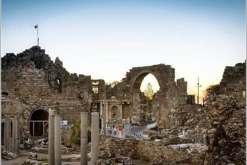 Ancient ruins with stone arches and columns, a flag on top, and a road in the foreground. 5