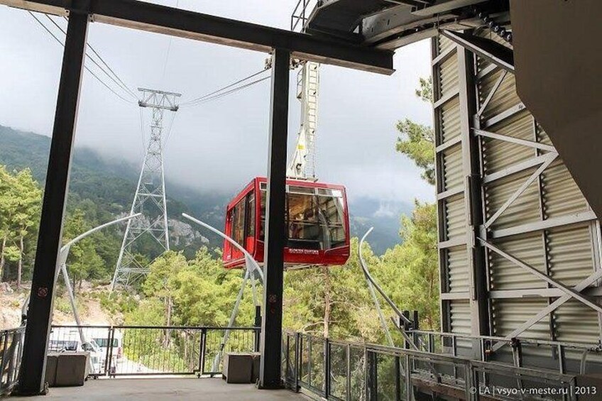 A red cable car suspended between two metal structures with a mountainous landscape in the background. 5
