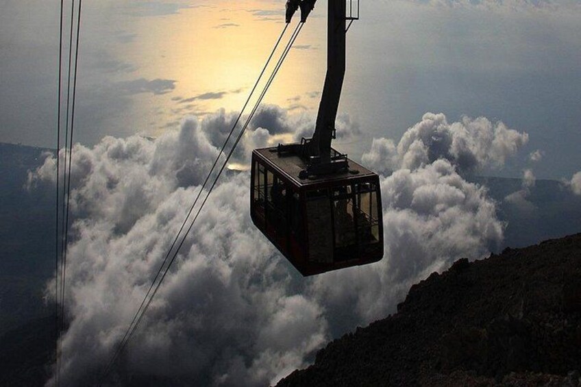 A cable car suspended above clouds with a mountain in the background. 1