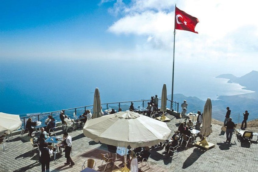 A coastal terrace with people, tables, umbrellas, and a flag. 3