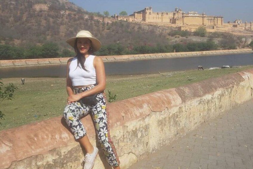 Una persona sentada en un muro de piedra junto a un río, con una fortaleza histórica al fondo. 4