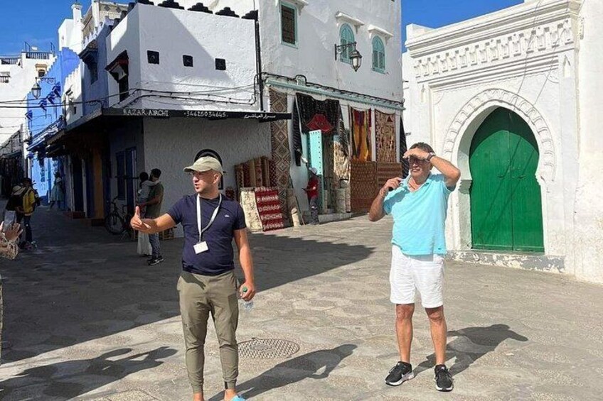 Two men walking on a street with buildings and a green door. 4