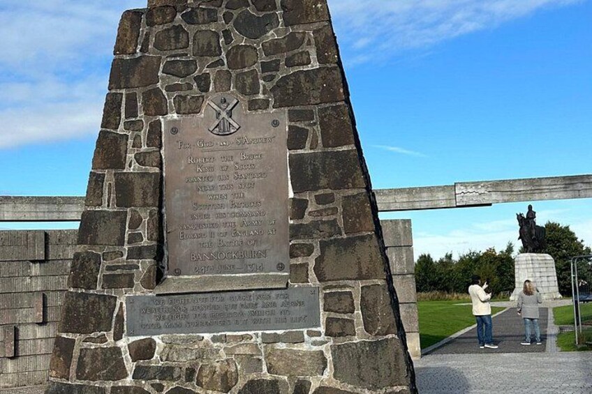 Een stenen monument met een plaquette, een standbeeld en een gazon. 3