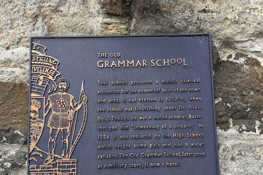 Een historische plaquette op een stenen muur, die de geschiedenis van The Old Grammar School beschrijft, inclusief de stichting in 1787-88 en de vervanging in 1856. 4
