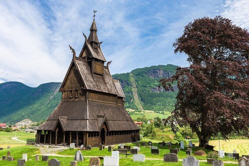 A wooden church with a steep roof and a bell tower, surrounded by a cemetery with gravestones. 1