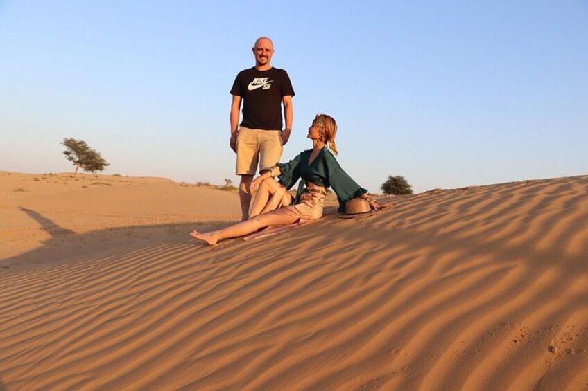 A desert landscape with sand dunes, a person standing, and another person lying on the sand. 2