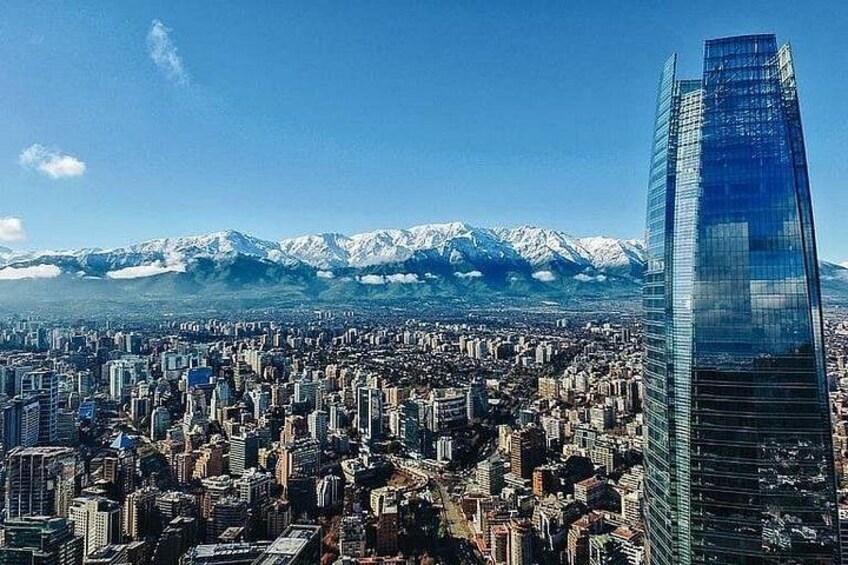 A cityscape with a prominent skyscraper, a dense urban area, and snow-capped mountains in the background. 1