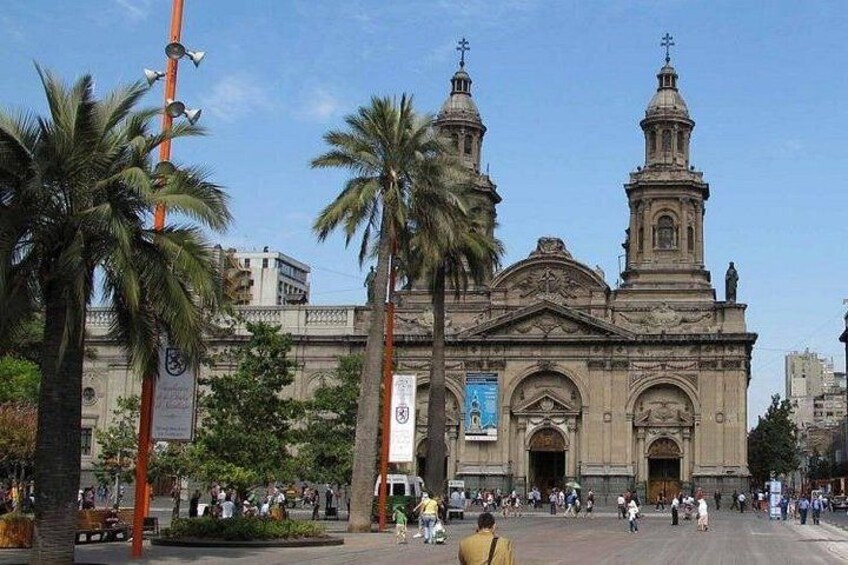 Un edificio histórico con dos torres, palmeras y una plaza animada con gente. 5