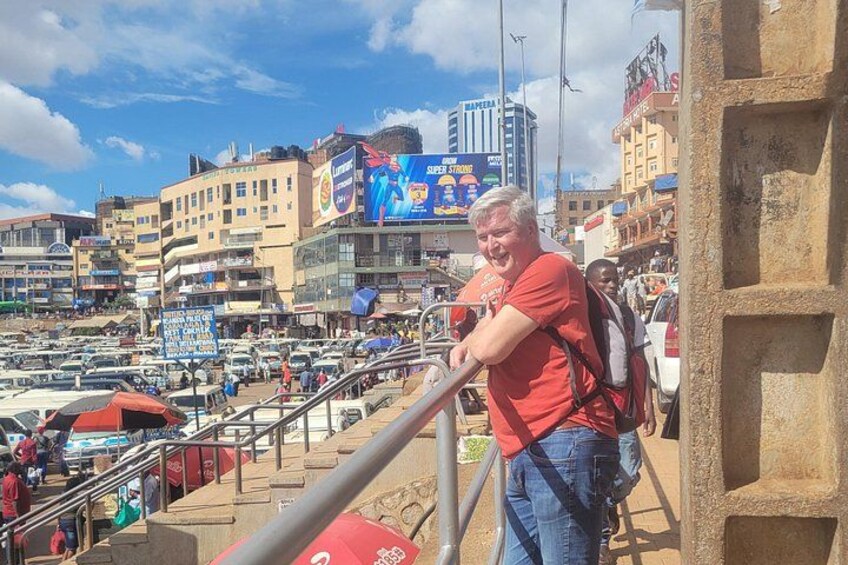 Una concurrida calle urbana con un hombre de pie en una escalera, edificios y un gran cartel publicitario al fondo. 4