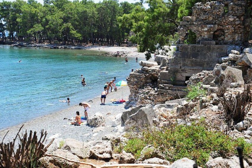 A beach with people swimming and sunbathing, rocky terrain, and trees in the background. 1