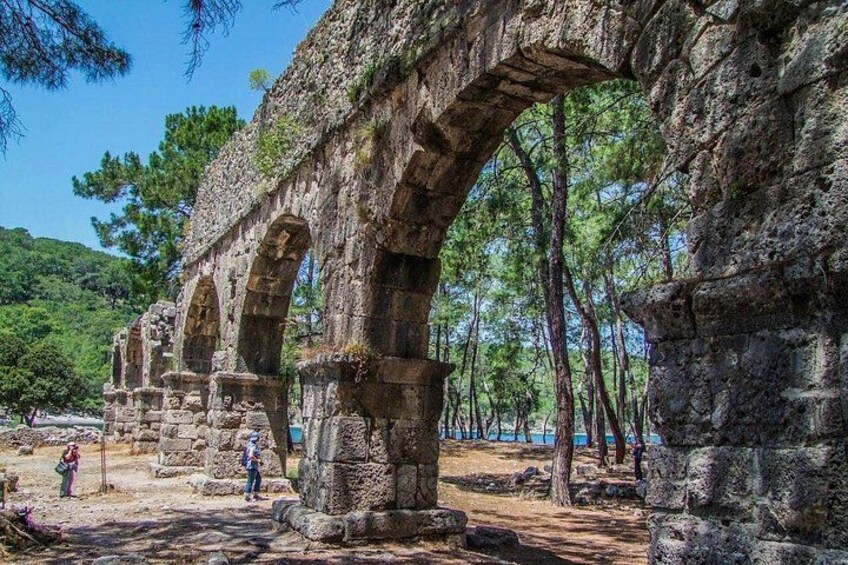 Ancient stone arches, a forested hillside, and a clear sky. 3