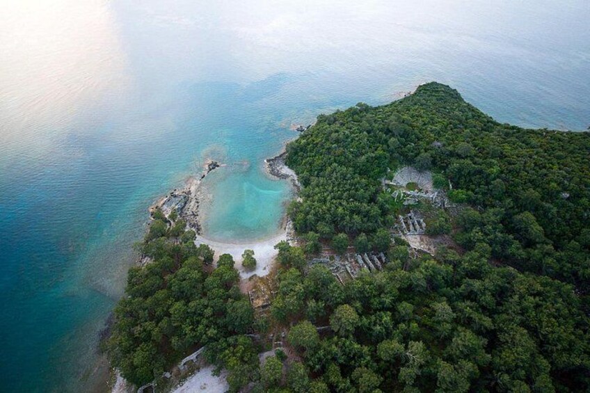 An aerial view of a coastal area with a clear turquoise bay surrounded by dense green forest and rocky outcrops. 5