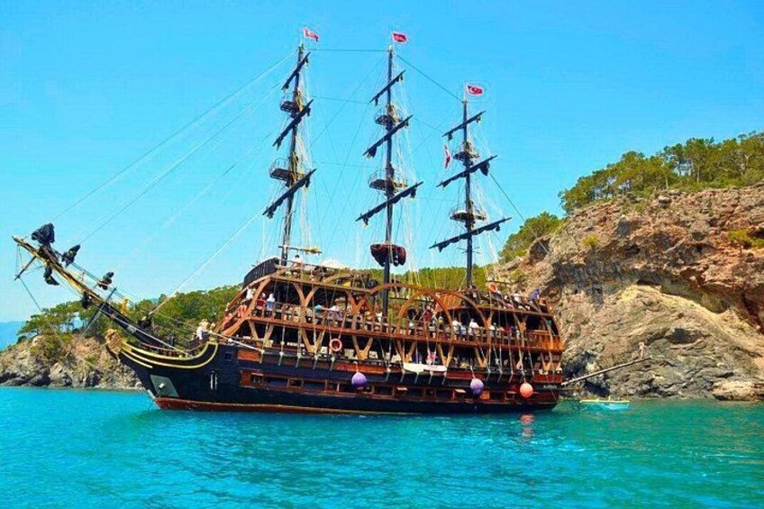 Un gran barco de madera con varios mástiles y velas amarrado a una costa rocosa. 1