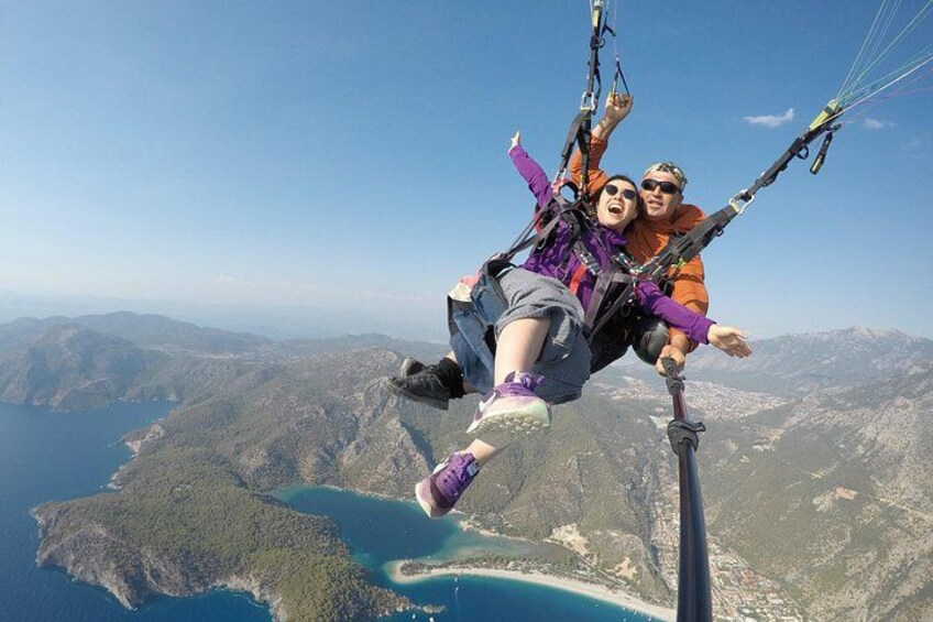 Two people paragliding over a mountainous landscape with a body of water below. 1