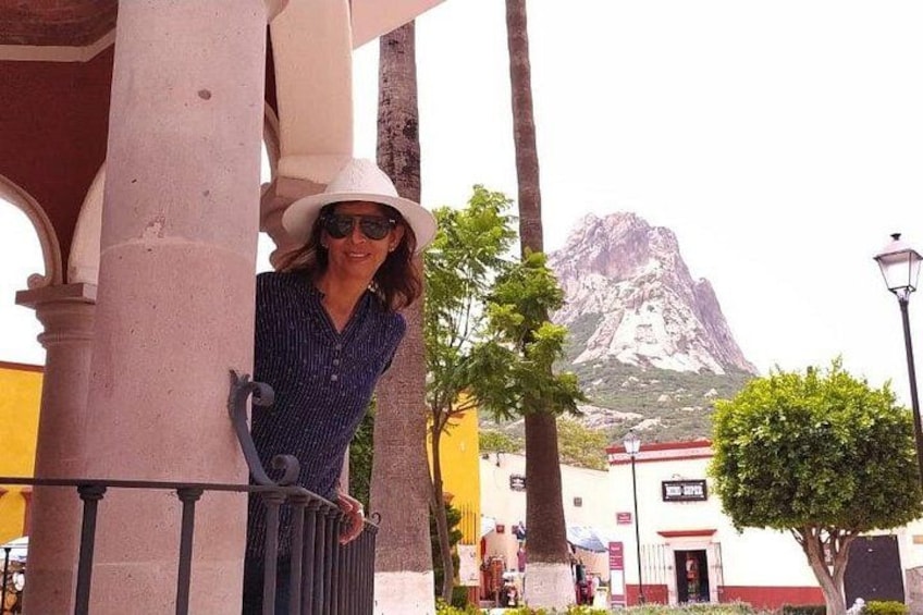 A person leaning on a column, a mountain in the background, and a building with a red roof. 2