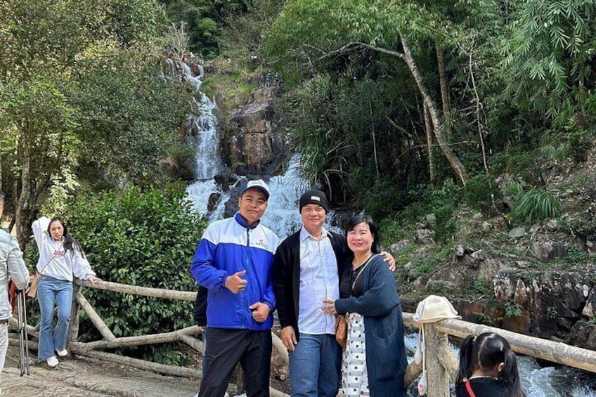 A group of people standing on a wooden bridge with a waterfall in the background. 2