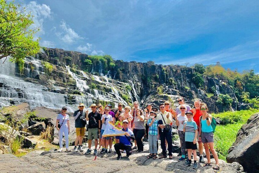 A group of people standing in front of a waterfall with a rocky landscape in the background. 1