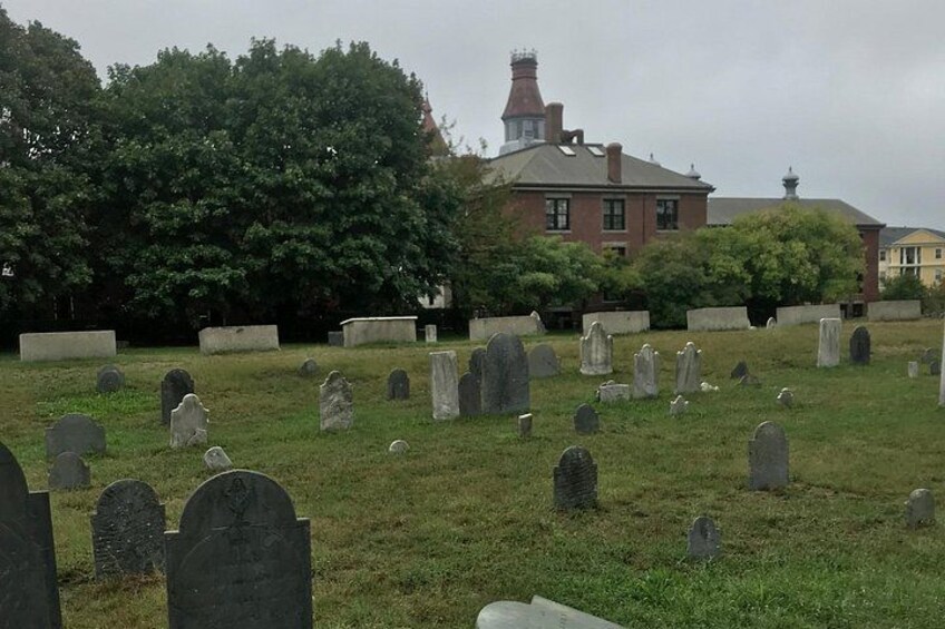 Ein Friedhof mit vielen Grabsteinen, einem großen Baum und einem Gebäude im Hintergrund. 2