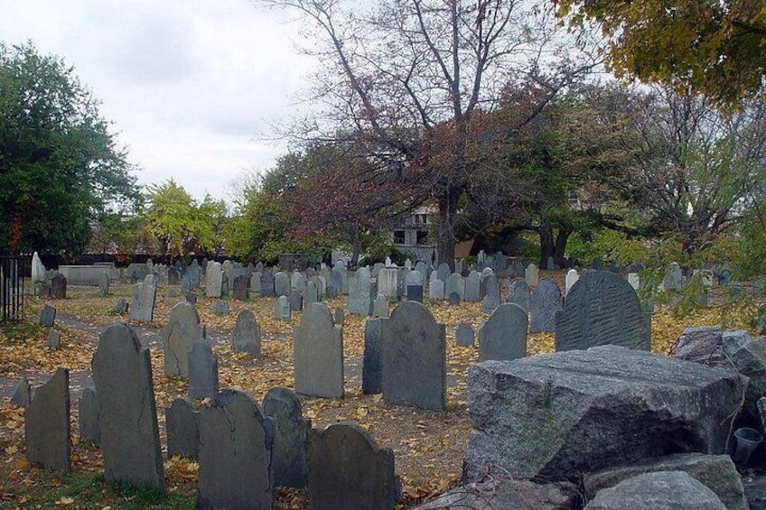 Ein Friedhof mit vielen Grabsteinen, Bäumen und einem Gebäude im Hintergrund. 3