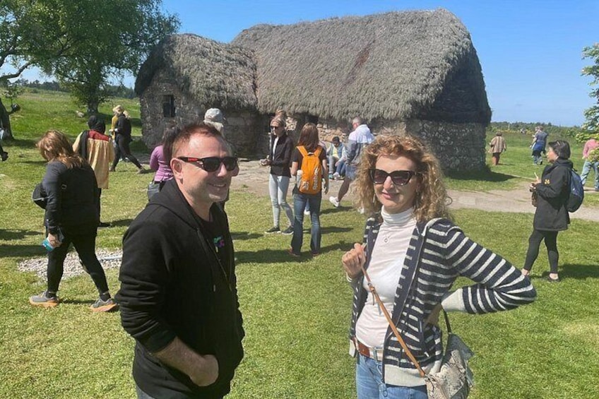 Un groupe de personnes se trouve sur un site historique, où se dressent des bâtiments aux toits de chaume. 3