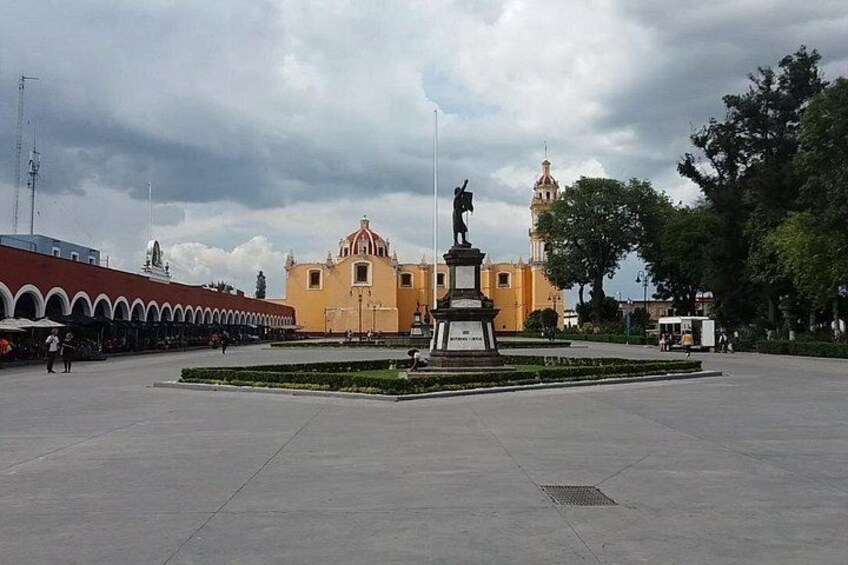 Una plaza con una estatua, un edificio amarillo y una torre. 4