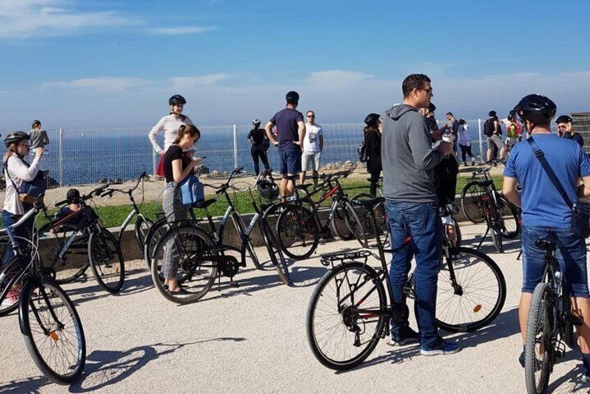 People standing near bicycles on a coastal path with a view of the sea. 3