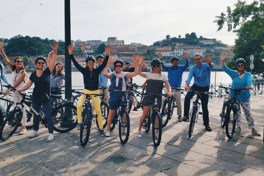 A group of people on bicycles by a waterfront with a cityscape in the background. 1