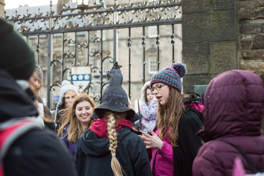 A group of people in winter clothing, some wearing hats, gathered in front of a wrought iron gate. 3