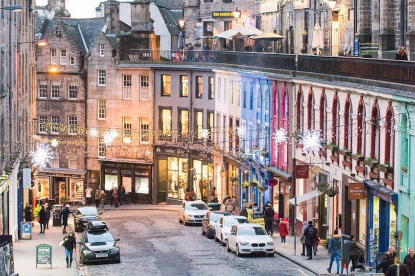 A cobblestone street lined with colorful buildings, cars parked along the side, and people walking. 2