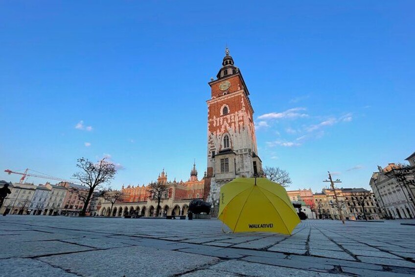 A historic tower with a clock, a yellow umbrella labeled 'WALKATIVE' in the foreground, and a clear blue sky. 3