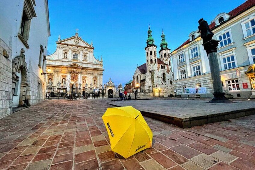 A historic building with a large facade and two green spires, a yellow umbrella on the ground, and a statue in the foreground. 2