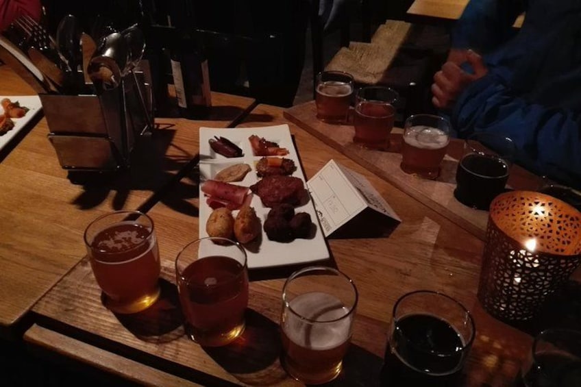 A wooden table with a plate of food, glasses of beer, and a candle. 1