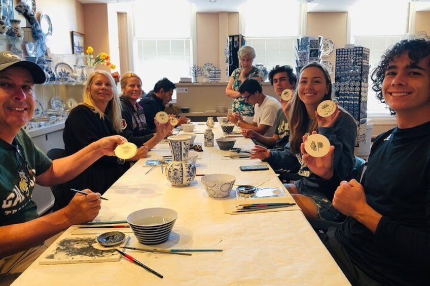 En grupp människor sitter runt ett bord och deltar i en aktivitet där de skapar föremål av keramik. 5
