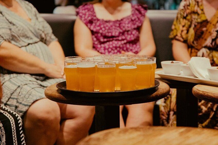 A tray with multiple glasses of amber liquid, likely beer, on a table in a social setting. 1