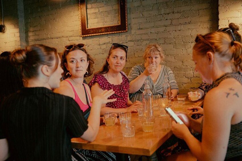 Un grupo de personas sentadas alrededor de una mesa de madera en un ambiente rústico, con paredes de ladrillo y un cuadro en la pared. 3