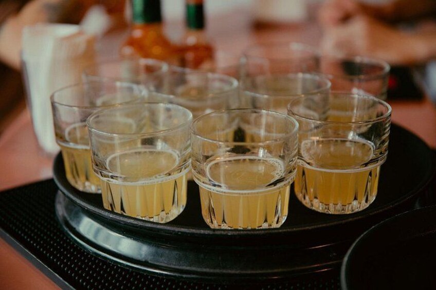 Una bandeja con copas para shots llenas de un líquido amarillo, posiblemente una bebida, sobre una bandeja negra. 5