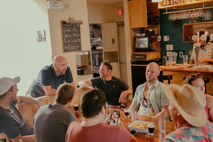 Un grupo de personas sentadas alrededor de una mesa en un restaurante, con un menú en una pizarra y una zona de bar al fondo. 4