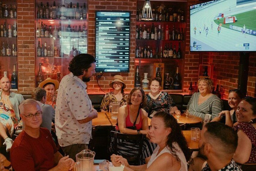 A bar with patrons seated at tables, a TV screen displaying a sports event, and shelves stocked with bottles. 3