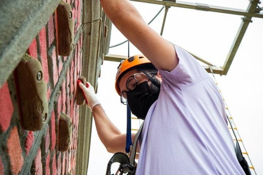 A person wearing a safety helmet and harness, working on a brick wall. 3