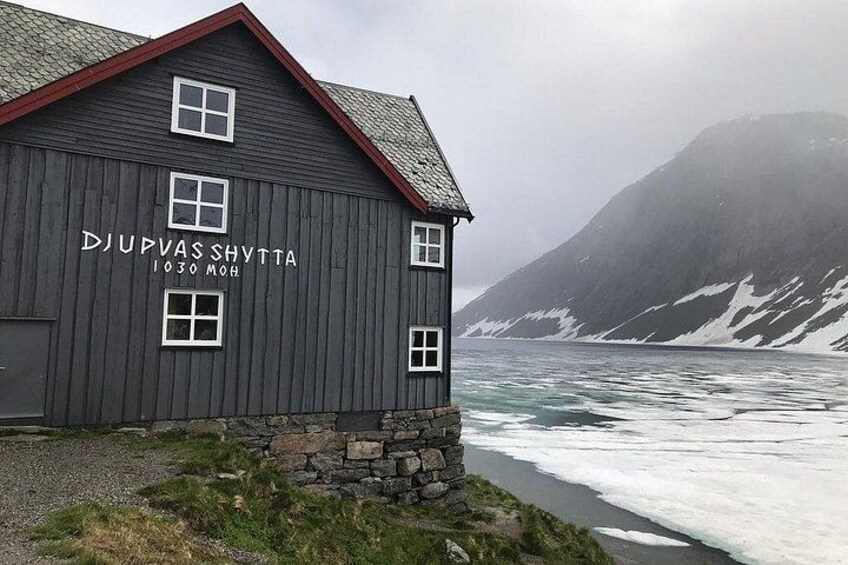 A wooden building with the inscription 'DJUPVAS SHYTTA 1030 MÖH' near a glacier. 2