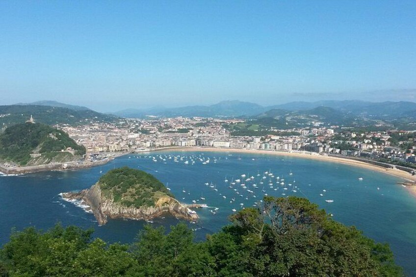 Un paysage urbain côtier avec une baie, des bateaux et une colline imposante surmontée d’une tour. 1