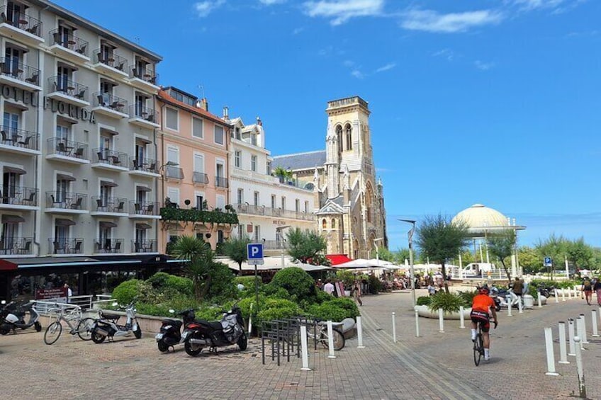 A city square with a historic church, parked bikes, and a cyclist. 1