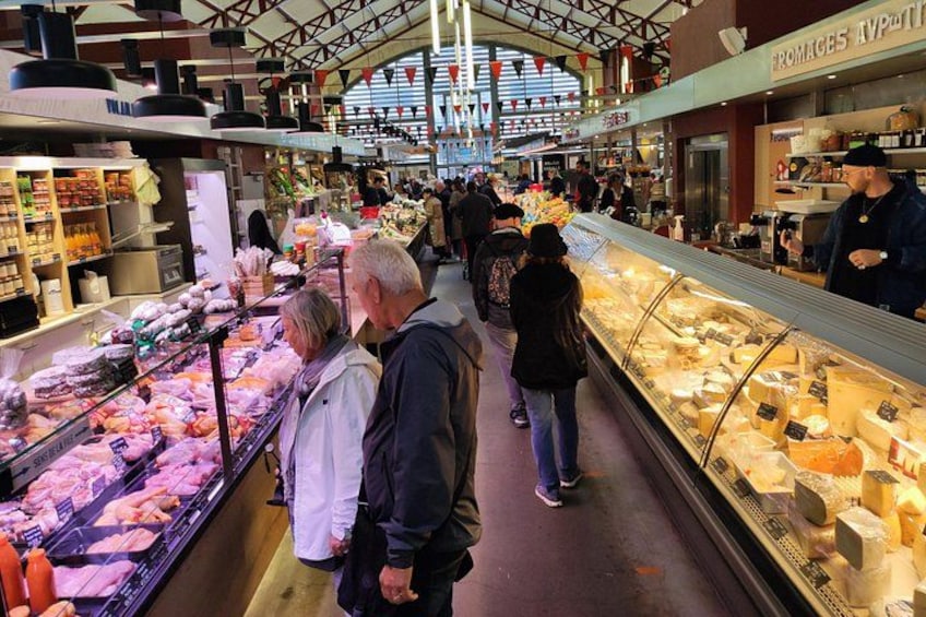 Ein überdachter Markt mit Menschen, die verschiedene Lebensmittel betrachten. 3