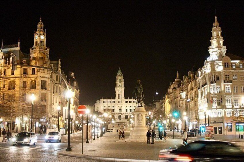 Une place de ville illuminée la nuit, avec des bâtiments historiques, une statue et des feux de signalisation. 3